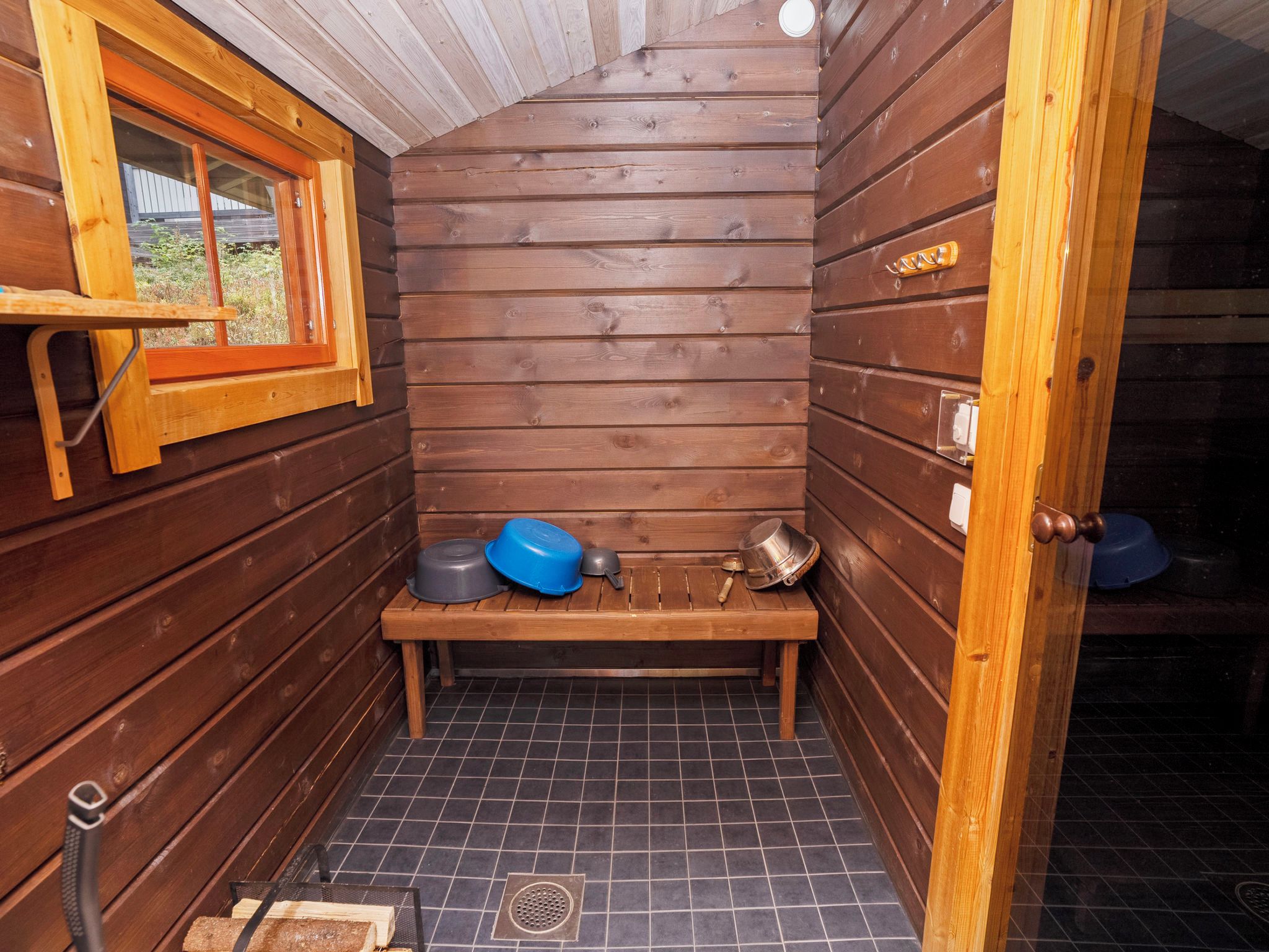 A small, wooden sauna room with a bench, a window, and a door.
