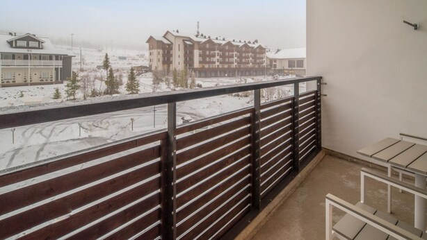 Un balcon doté d’une rambarde en métal, donnant sur un paysage enneigé et des immeubles d’habitation.