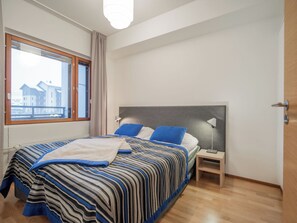 Ein Schlafzimmer mit Bett, Nachttisch, Lampe und einem Fenster mit Blick auf Gebäude.