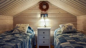 Un dormitorio abrigado en el ático con dos camas, paredes de madera, una mesita de noche pequeña y una corona decorativa.