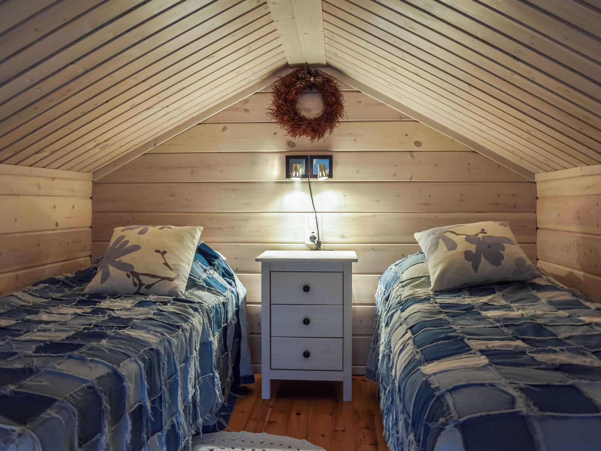 A cozy attic bedroom with two beds, a nightstand, and a wall-mounted light fixture.