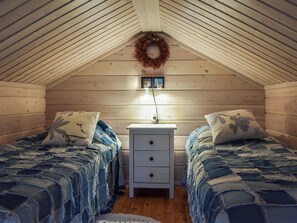 A cozy attic bedroom with two beds, a nightstand, and a wall-mounted light fixture.