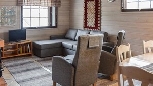 Una sala de estar con un sofá modular, dos sillones, una mesa de madera y un televisor sobre un mueble.
