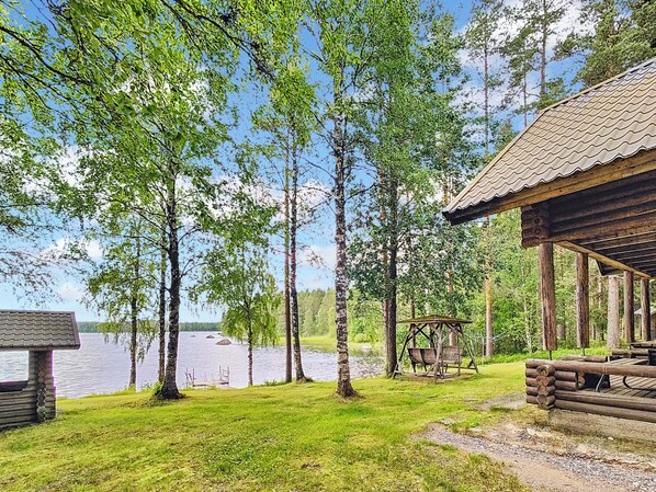 Una cabaña con terraza de madera y una silla mecedora con vistas al lago.