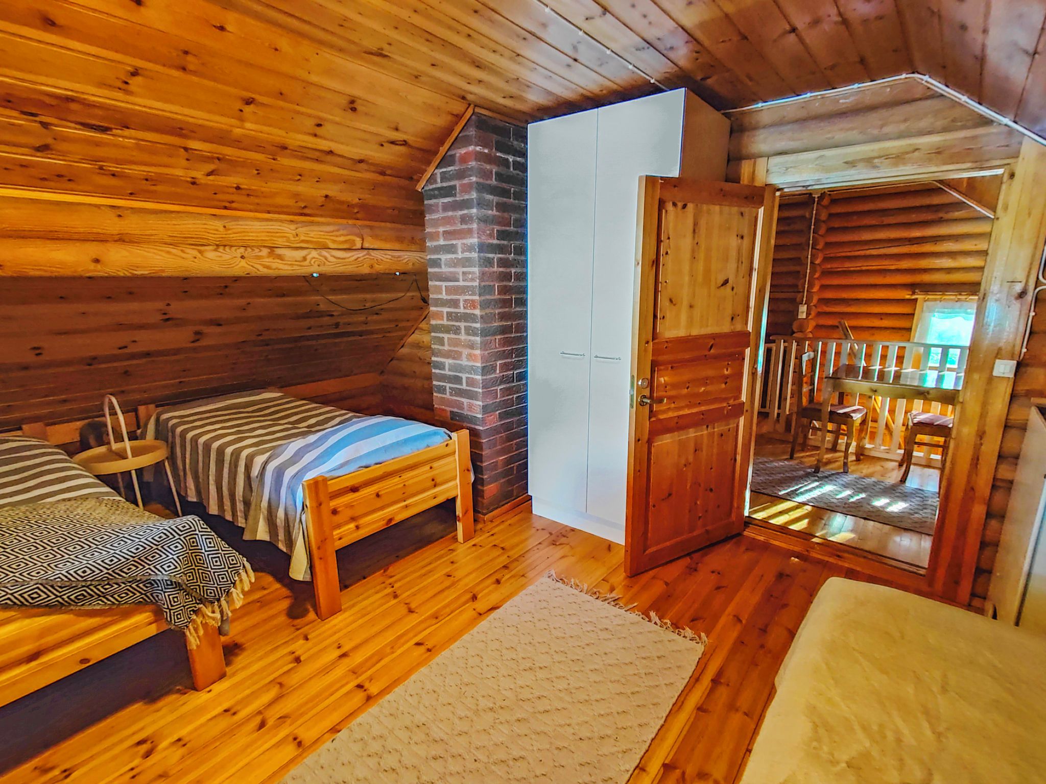 Una cabaña acogedora con interior de madera, una cama, una mesita y una puerta que da a un balcón.