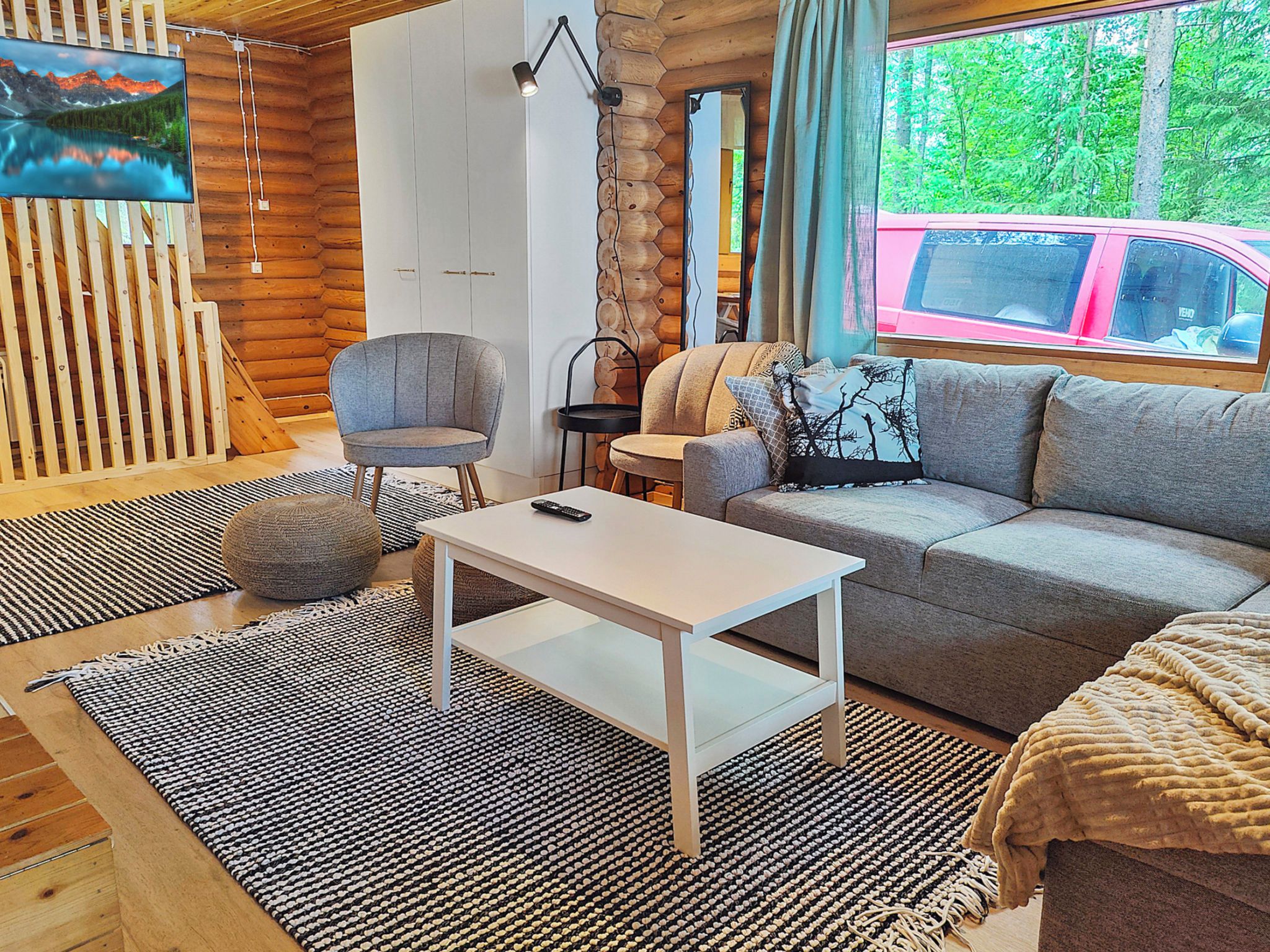 A cozy cabin interior with a sofa, armchair, and a television mounted on a wooden wall.