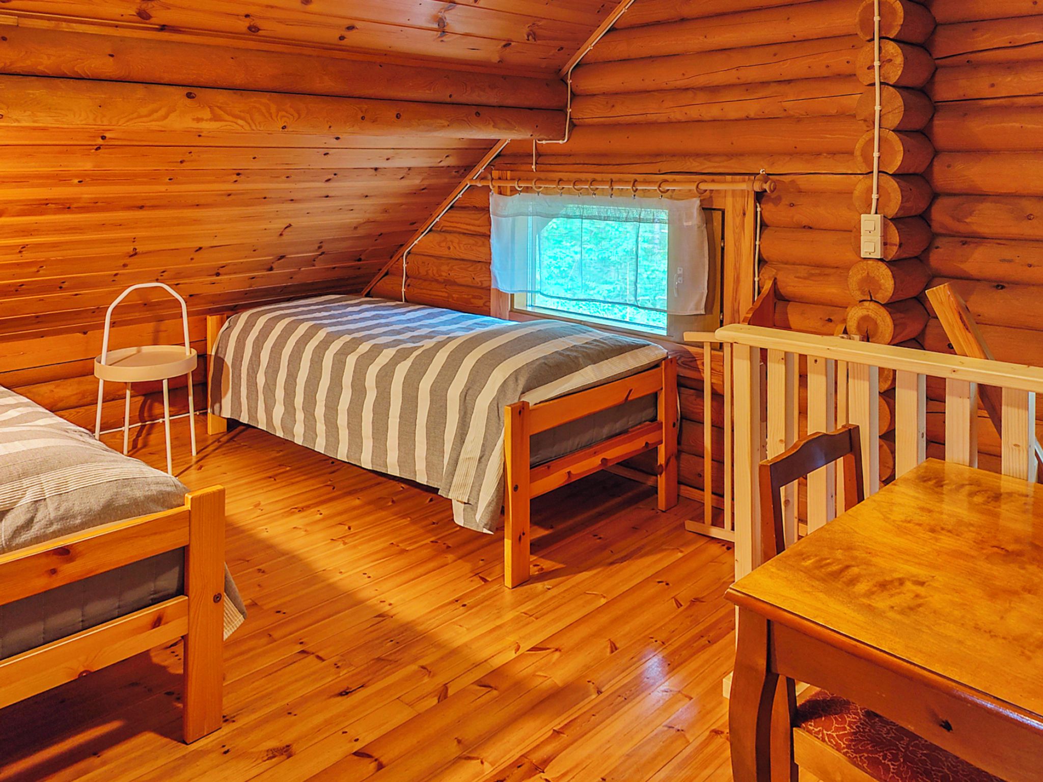 Interior de una cabaña con una cama, una mesita, una silla y un ventanal con vistas.