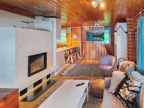 A cozy cabin interior with a fireplace, wooden walls, a dining area, and a comfortable seating space. - Koivula by Interhome (Soini)