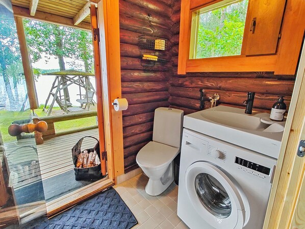 A compact cabin with a wooden interior, a toilet, a washing machine, and a small sink.