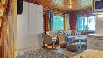 A cozy cabin interior with a wooden ceiling, a sofa set, a dining table, and a TV mounted on the wall.