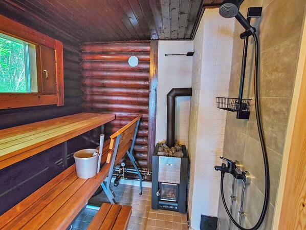 A wooden interior with a bench, a stove, and a shower.