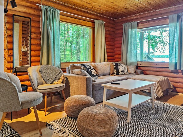 A log cabin interior with a sofa, chairs, a coffee table, and large windows with curtains. - Koivula by Interhome (Soini)
