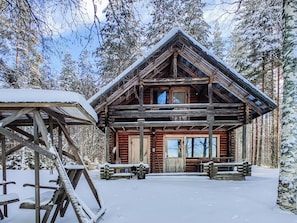 Una cabaña de madera con techo a dos aguas, rodeada de árboles cubiertos de nieve.