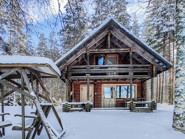 Una cabaña de madera con techo a dos aguas, rodeada de árboles cubiertos de nieve.