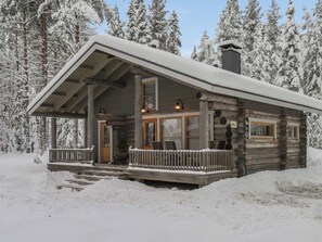 Hirsimökki, jossa on kuisti, suuret ikkunat ja savupiippu.
