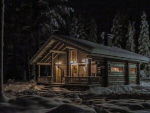 A log cabin with a porch, a chimney, and a snow-covered landscape.