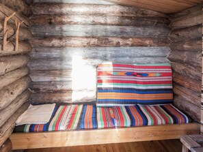 A log cabin interior with a wooden bench and a colorful striped blanket.