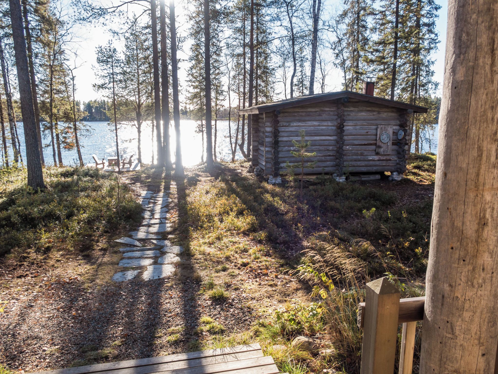 Mökki, jonka luo johtaa kivipolku, ja jonka ympärillä on puita ja vesistö.