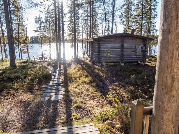 A cabin with a stone path leading to it, surrounded by trees and a body of water.