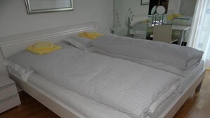 Un llit doble amb estructura blanca i roba de llit gris, una taula de nit i un mirall a la paret.