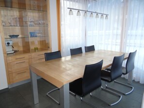 Ein Konferenzraum mit Holztisch, schwarzen Stühlen, einer Glasvitrine mit Gläsern und einem Fenster mit Vorhängen.