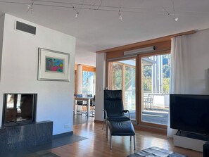 Een moderne woonkamer met een open haard, een televisie en een eethoek met veel daglicht.