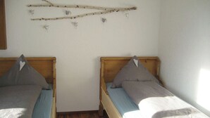 A room with two single beds, wooden headboards, and a wall-mounted decoration of branches and hearts.