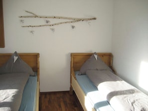 Una habitación con dos camas individuales, cabeceros de madera y un adorno en la pared con ramas y corazones.