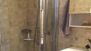 Un baño con ducha envuelta en vidrio, un lavamanos blanco y una pared de azulejos con diseño floral.