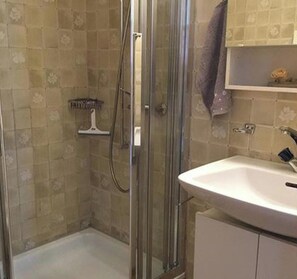 Un baño con ducha envuelta en vidrio, un lavamanos blanco y una pared de azulejos con diseño floral.