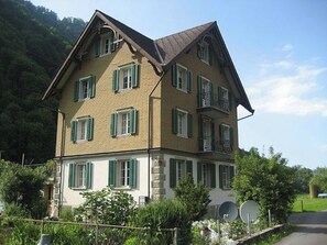 Una casa de varios pisos con un tejado a dos aguas pronunciado, numerosas ventanas con contraventanas y una base de piedra.