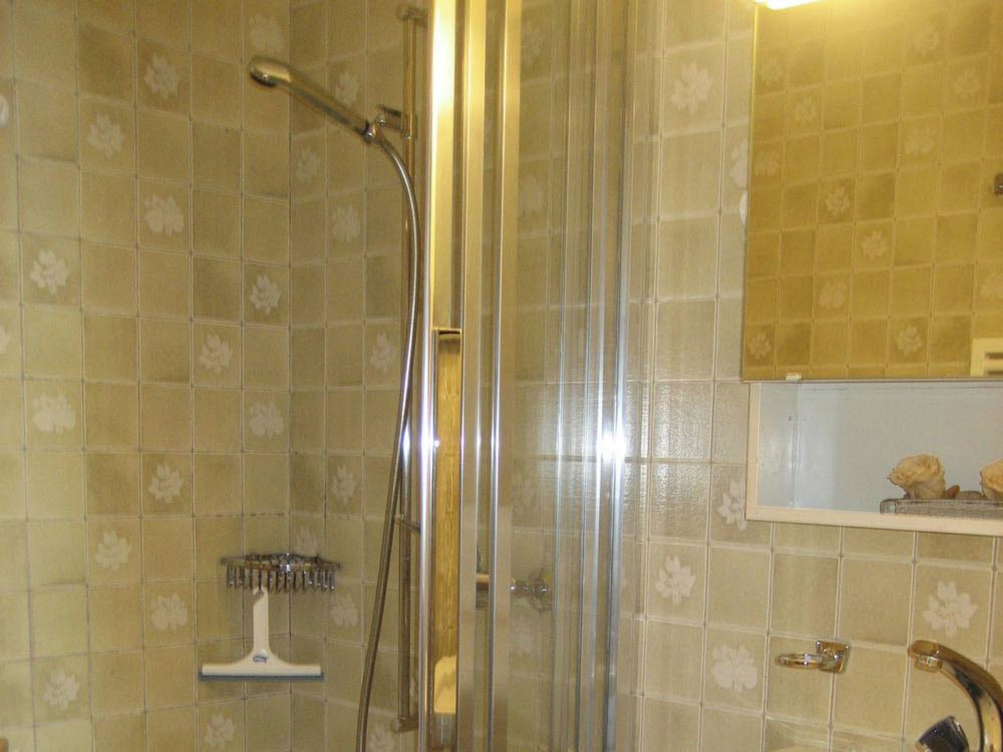 Un espace douche doté d  ’une porte en verre, d’un sèche-mains et d’un mur carrelé orné d’un motif floral.