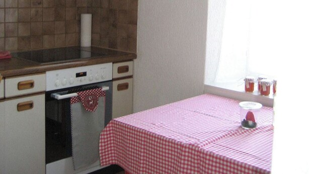 A kitchen with a checkered tablecloth, a stove, and a window with curtains.