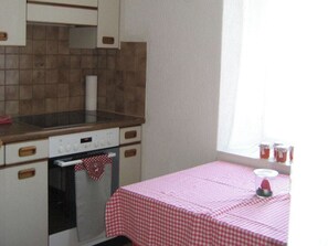 Una cocina con mantel a cuadros, estufa y ventana con cortinas.