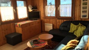 A cozy cabin interior with a black leather sofa, a wooden entertainment unit with a television, and a small round table.