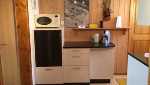 A compact kitchen with wooden paneling, a microwave, a coffee maker, and a small refrigerator.