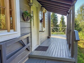 A wooden deck with a covered porch, a window with a basket of flowers, and a door.