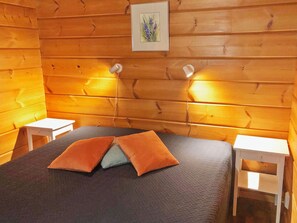 A wooden-paneled room with a bed, two bedside tables, and a wall-mounted light fixture. - Joutsen a by Interhome (Kuusamo)