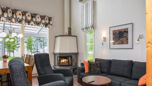 A modern living room with a fireplace, grey sofas, and a dining area with a table and chairs. - Paltamon golfhovi a (sis. 2 golf pelioik by Interhome (Paltamo)