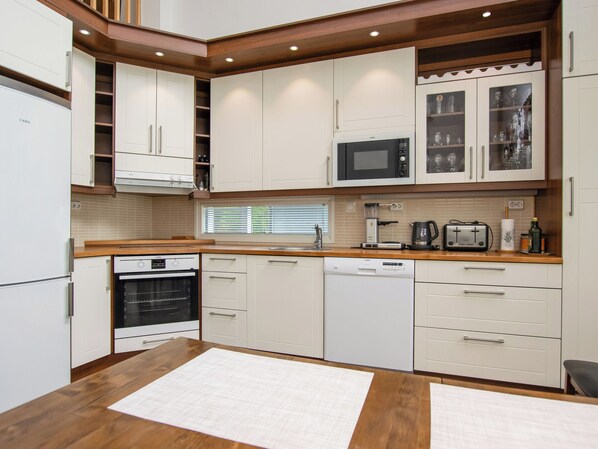 Una cocina moderna con armarios blancos, horno empotrado, microondas y cafetera.