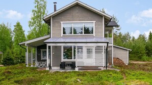 A two-story house with a covered patio, a chimney, and a stack of firewood. - Paltamon golfhovi a (sis. 2 golf pelioik by Interhome (Paltamo)
