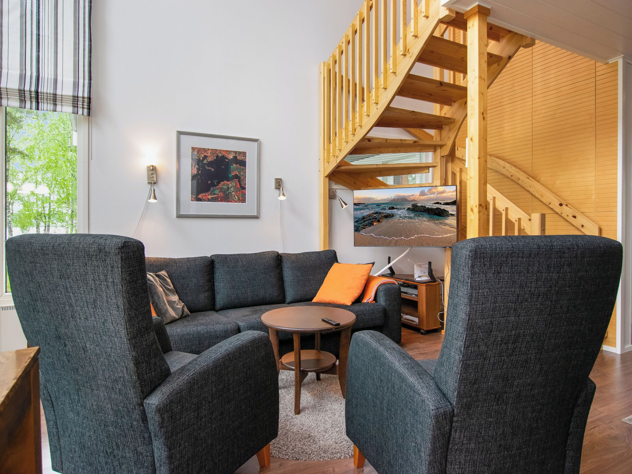 A modern living room with a sectional sofa, a small round table, and a wooden staircase.