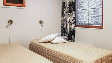 A bedroom with a bed, two bedside tables, a window with a view of buildings, and a curtain with a cityscape design.