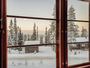 Une fenêtre donnant sur un paysage enneigé, avec des arbres à feuilles persistantes et un chalet en bois.