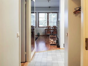Un couloir menant à une pièce dotée d’un plancher en bois, d’une fenêtre et d’un porte-manteau.