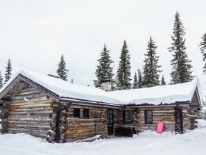 A rustic log cabin with a snow-covered roof, surrounded by tall evergreen trees. - Hopukka a2 by Interhome (Sodankylä)