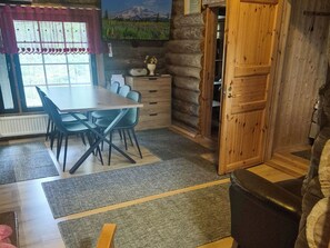 A room with a dining table, chairs, a wooden cabinet, a radiator, and a window with a view of a mountain landscape. - Hopukka a2 by Interhome (Sodankylä)