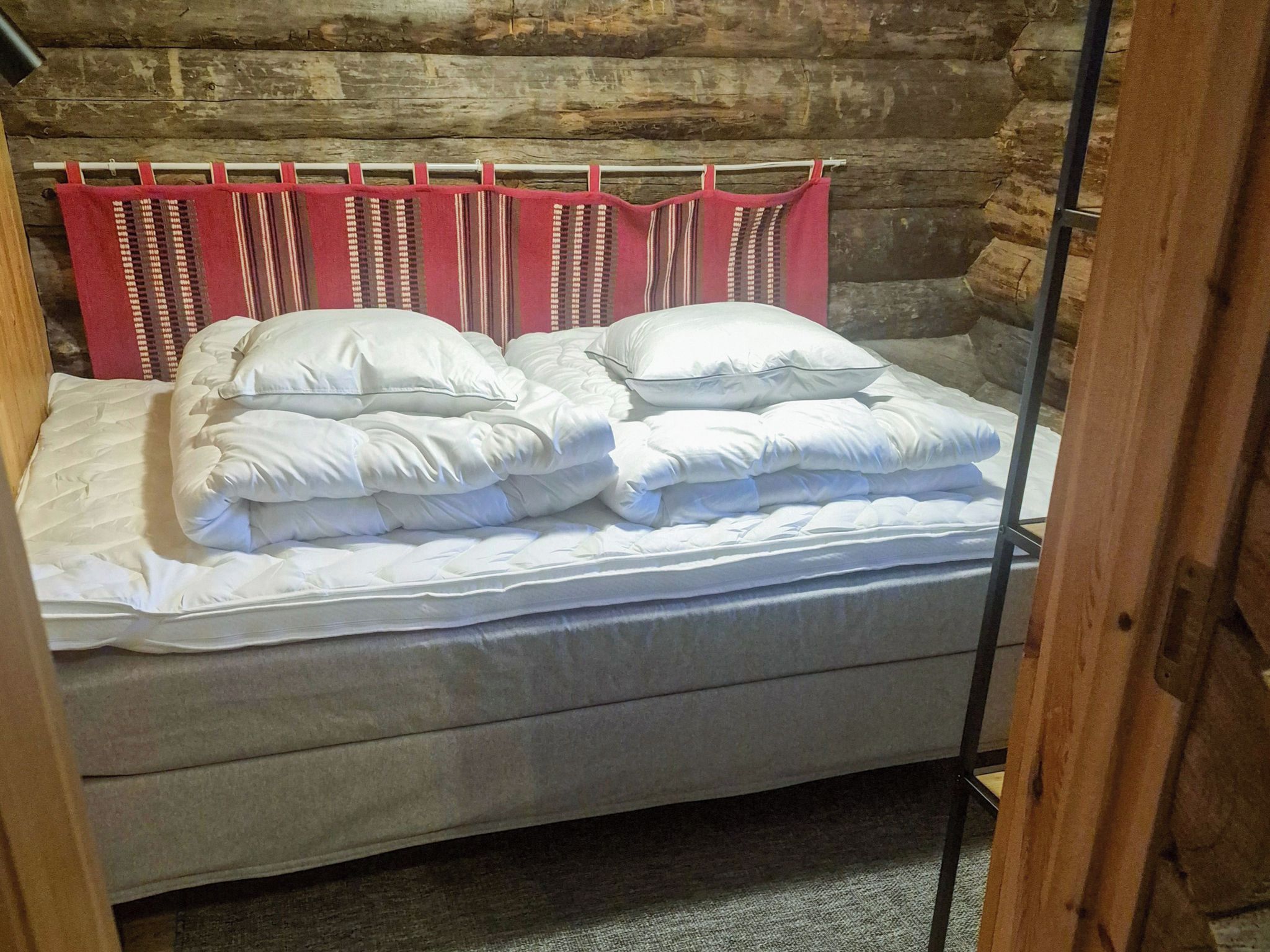 Ein Bett mit weißer Bettwäsche und Kissen, ein hölzernes Kopfteil und ein rot-weiß gestreifter Vorhang.