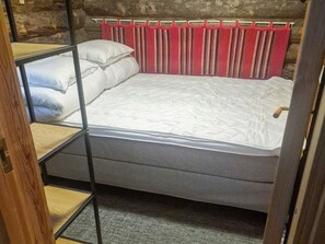 A bunk bed with a mattress and pillows, a wooden headboard, and a red curtain. - Hopukka a2 by Interhome (Sodankylä)