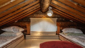 Un dormitorio acogedor en el ático, con techo inclinado, vigas de madera y una cama individual con una colcha roja.